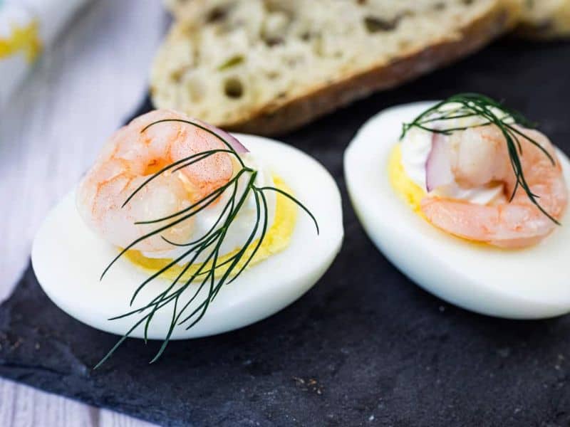 Two Pickled Shrimp Egg Shooter halves were placed on a slate board, next to slices of bread.